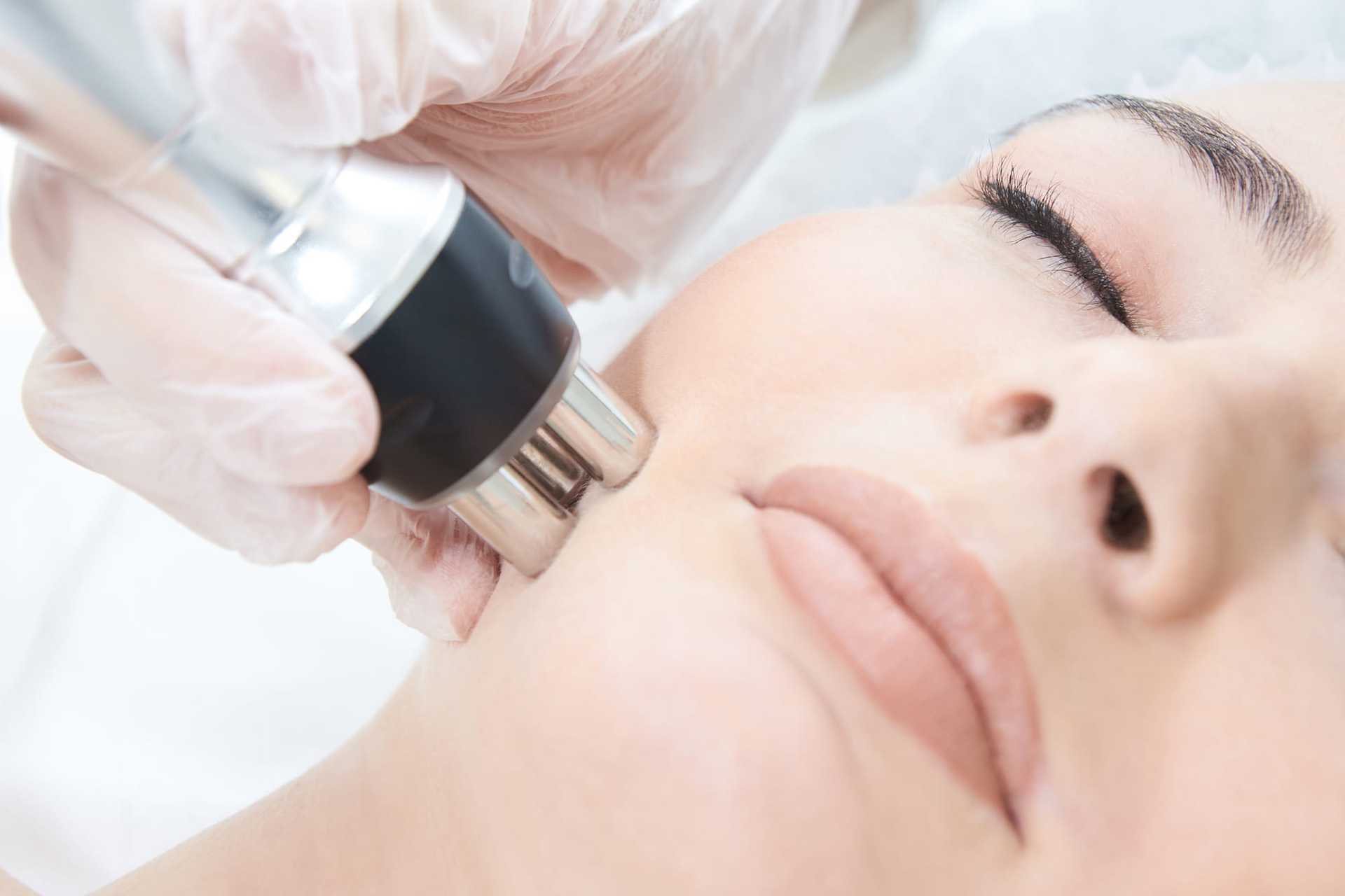Close-up of a facial treatment with a handheld beauty device on a woman's cheek.