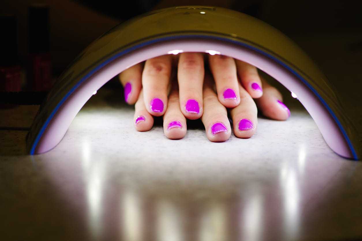 Nails with pink polish being cured under a UV lamp.