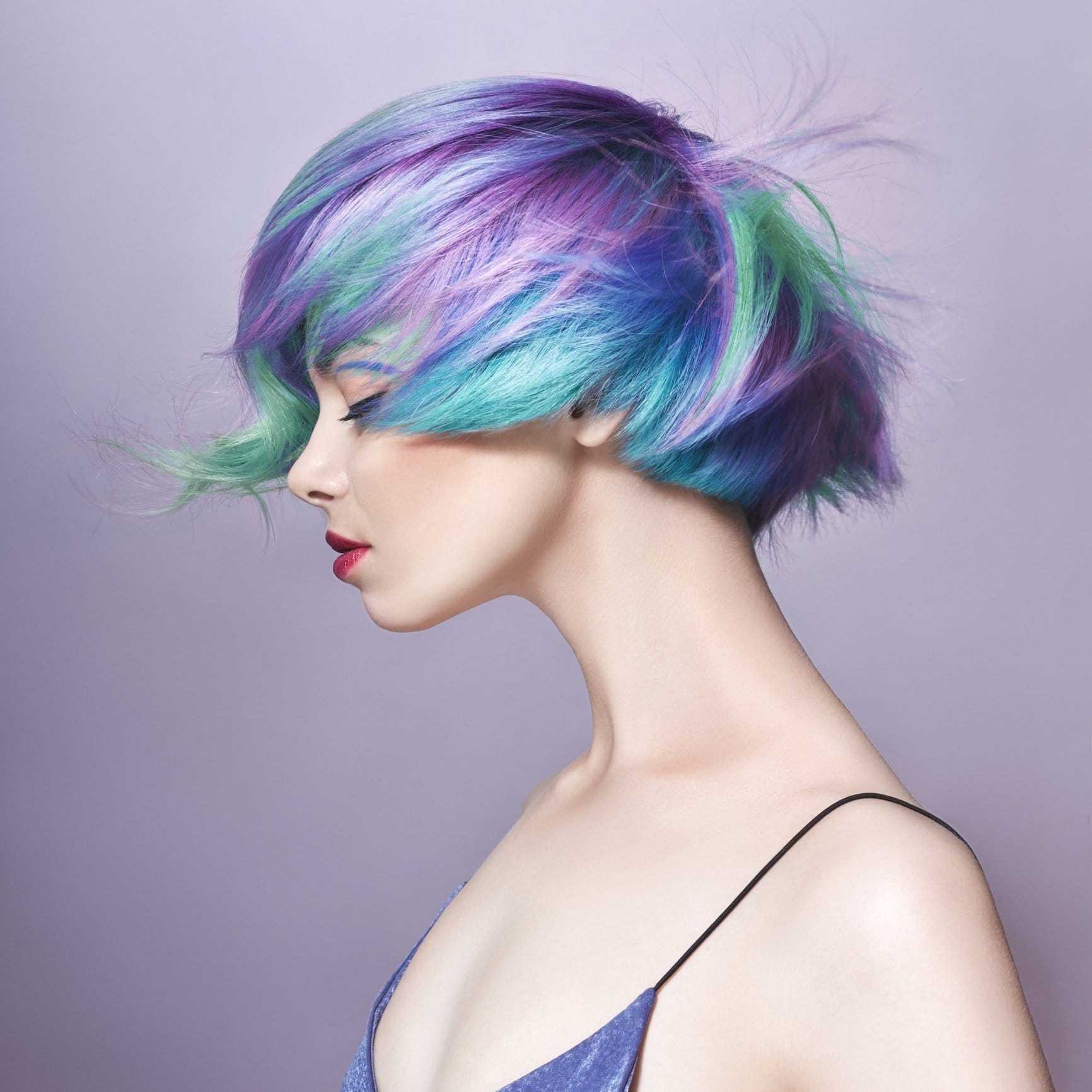 Woman with vibrant purple and green bob haircut on a lavender background.